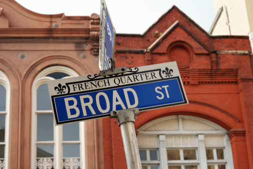 A street sign for Broad St in  downtown Charleston, SC with historic old buildings in soft focus background.